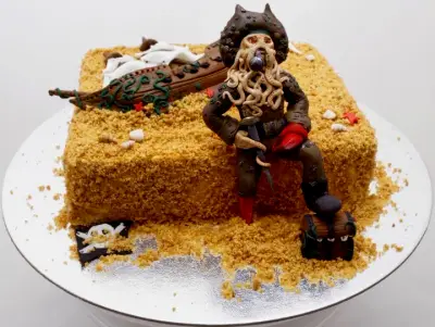 Square cake covered in golden crumb, with a tentacled pirate captain, a wrecked ship, treasure chest, shells, starfish and a skull flag.