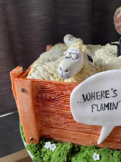 Close-up of a fondant sheep face in a wood-effect crate cake, beside a sign reading Where's Flamin'.