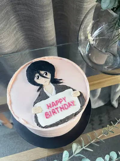 Pink cake hand-painted with a dark-haired character in a jacket holding a sign that reads Happy Birthday.
