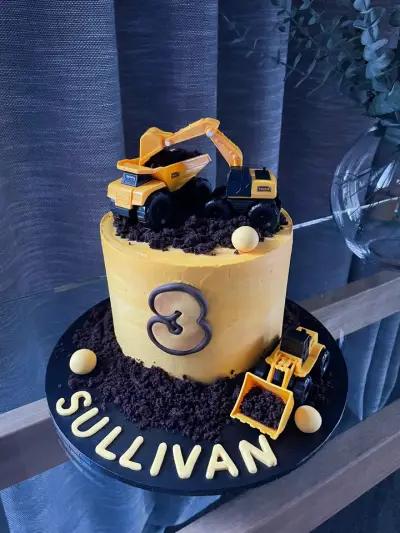Mustard cake with a chocolate number three, toy diggers in cookie-crumb dirt, and Sullivan spelled out on the board.