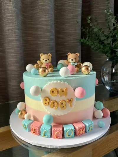 Pastel blue, yellow and pink cake with two fondant teddy bears, an Oh Baby plaque and Welcome spelled in coloured blocks.