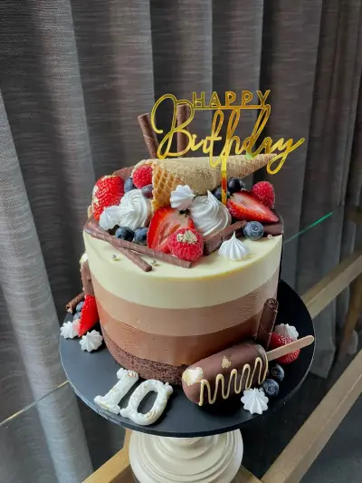Ombre chocolate drip cake topped with berries, meringues, a waffle cone and a Happy Birthday topper, with a number ten.