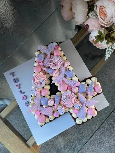 A cake shaped like the number 4, decorated with pink and lilac swirls, mermaid tails, shells and stars, and a name in fondant letters.