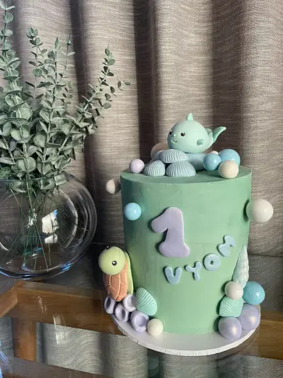 A mint-green cake topped with a fondant sea creature and turtle, shells and pearls, plus a purple number 1 and pale blue lettering.