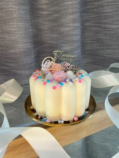 A cake of vertical cream finger biscuits topped with pastel meringue kisses, sprinkles and a gold Happy Birthday topper.