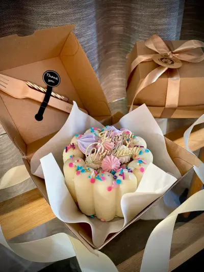 A cream finger-biscuit cake with meringue kisses and a Happy Birthday topper, packaged in a gift box with wooden cutlery.