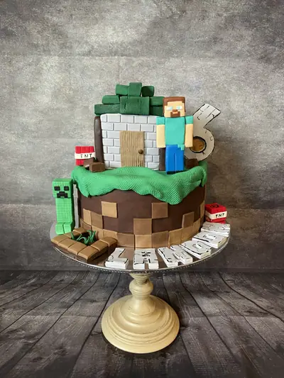 Minecraft-themed sixth birthday cake with block-textured brown sides and green grass top, a block house, Steve, Creeper, TNT blocks, a large number 6 and the name Liam.