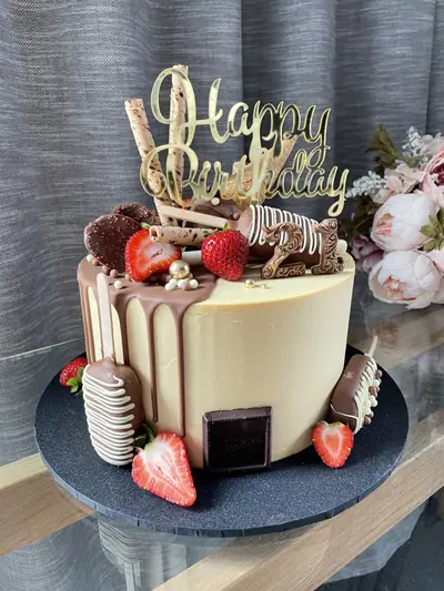 Round 21st birthday cake with ivory buttercream, milk chocolate drip, strawberries, cakesicles, wafer rolls, chocolate discs, gold pearls and a gold birthday topper.