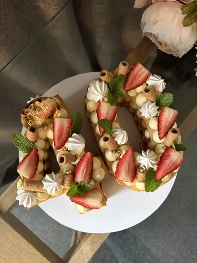Number 40 cake with cream-filled golden layers, sliced strawberries, mint leaves, white meringues, wafer rolls and metallic gold sugar pearls.