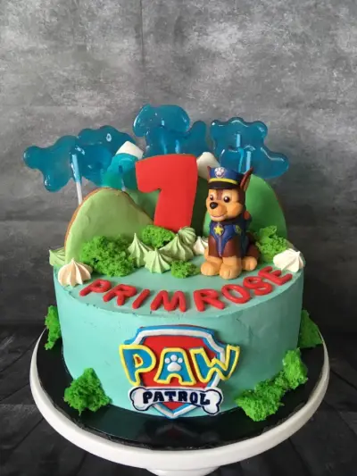 Mint-green cake with a Paw Patrol police-dog figure, a red '7', blue candy shards, a piped name on top, and a Paw Patrol logo.