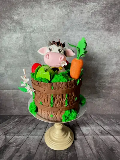 Cake styled as a wooden barrel filled with green foliage, a cabbage, tomato, and carrot, topped with a cow figure.