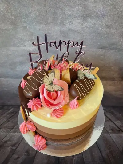 Ombre cake with chocolate-dipped treats, a pink rose, meringue kisses, green butterflies, and a chocolate 'Happy Birthday' script.