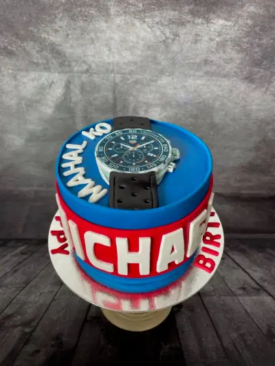 Blue and red cake topped with a realistic watch model, with 'Happy Birthday' and personalised lettering.