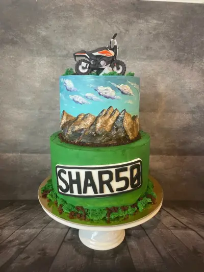 Two-tier cake with a painted mountain and sky mural, a dirt bike topper, and a green tier reading SHAR50.