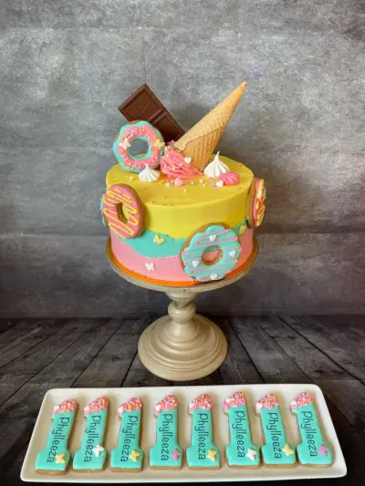 Yellow, teal and pink cake with donut cookies, a wafer cone and chocolate bar, served with number-one cookies reading Phyllieza.