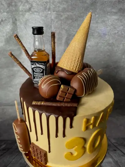 Gold drip cake topped with a mini spirits bottle, chocolate truffles, pretzel sticks and a dipped wafer cone, reading Happy 30.