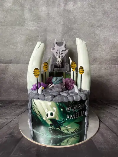 Dark video-game themed cake with sculpted tusks, a horned throne figure, lantern picks, and edible print reading Hollow Knight, Amelia.