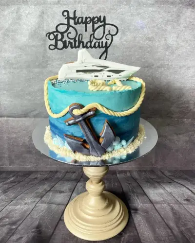 Teal ombre cake with a piped rope border, a fondant anchor, an edible yacht image, and a Happy Birthday topper.