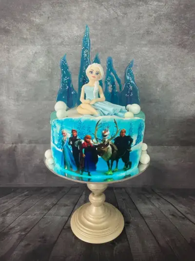 Blue ice-themed cake with a fondant princess figure among ice shards, and a printed scene of characters with a reindeer.