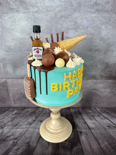 A teal drip cake with a miniature bourbon bottle, chocolate truffles, a wafer cone, and 'Happy Birthday' in yellow letters on the side.