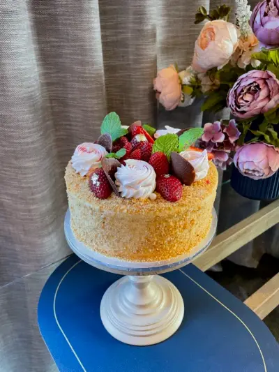 Round cake coated in crumbs and topped with meringue swirls, fresh strawberries, chocolate pieces and mint leaves.