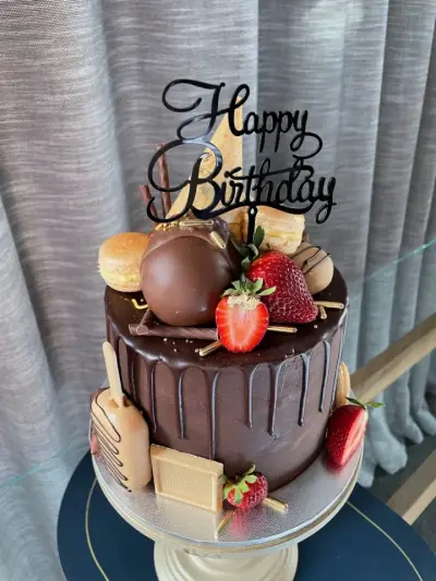 Dark chocolate drip cake topped with macarons, chocolate truffles, strawberries and a Happy Birthday topper.