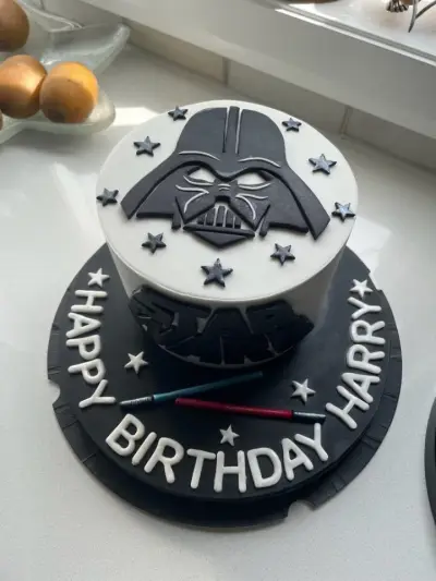 White and black Star Wars cake with a Darth Vader design, stars, lightsabers and Happy Birthday Harry lettering.