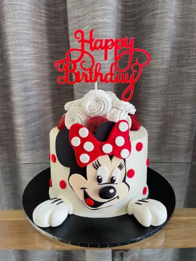 White cake with red polka dots, a Minnie Mouse face, white glove hands, strawberries and a red Happy Birthday topper.