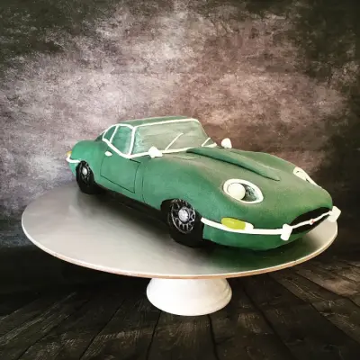 Cake sculpted and iced as a green vintage sports car with cream trim details and black wheels.