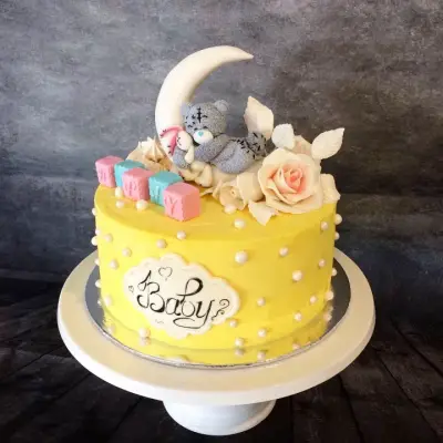 Yellow cake with pearl dots, a moon and teddy bear topper, pastel blocks, sugar roses and a plaque reading 'Baby'.