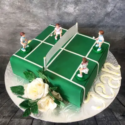 Square cake iced as a green table tennis table with a net, four player figurines and white sugar roses.