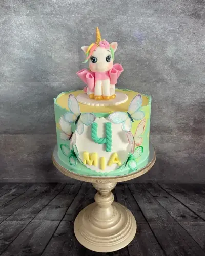Pastel green cake with wafer butterflies, a fondant unicorn on top, and a name plaque with the number 4.