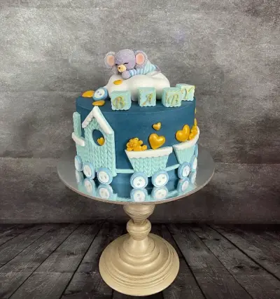 Teal cake shaped like a train, with a sleeping mouse figure, gold hearts, and blocks spelling 'BABY' on top.