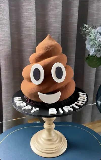 A brown swirled cake shaped like a smiling poop emoji, on a black board with 'Happy Birthday' in white letters.