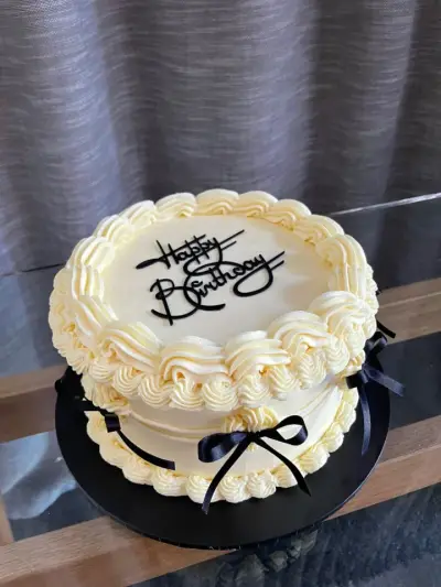Cream cake with piped shell borders, black ribbon bows, and a black 'Happy Birthday' topper.