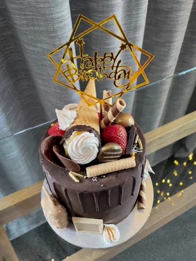 Dark chocolate drip cake with strawberries, meringues, gold chocolates, and a gold star-shaped Happy Birthday topper.