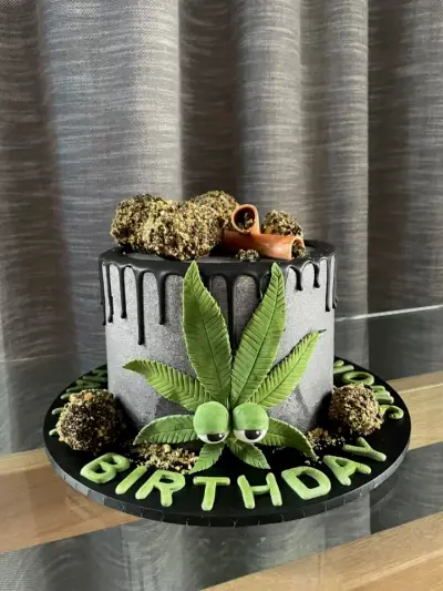 Grey textured cake with a chocolate drip, a large fondant cannabis leaf, bud-shaped chocolates, and 'Birthday' in green letters.