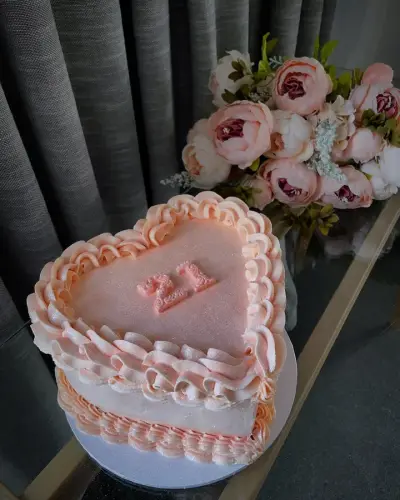 Heart-shaped cake with peach ruffled piping, a shimmering glitter top and a pink fondant number twenty-one in the centre.