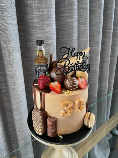 Caramel drip cake with a number thirty, topped with strawberries, chocolate truffles, a mini whisky bottle and Happy Birthday topper.