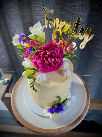 Pale buttercream cake decorated with fresh pink and white flowers, meringue kisses and a gold Twenty One topper.