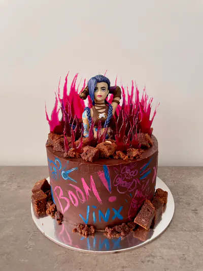 Tall chocolate League of Legends cake with a hand-sculpted and hand-painted edible Jinx figurine, blue braided hair, painted tattoos and clothing, translucent crimson sugar shards, chocolate rubble and pink-and-blue graffiti.