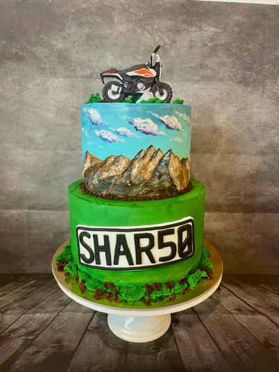 Two-tier green and turquoise motorcycle birthday cake with a hand-sculpted black, white and orange motorbike, hand-painted New Zealand mountains and clouds, edible landscape details and a SHAR50 number-plate design.